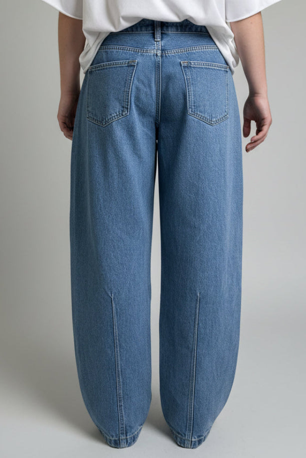 Person wearing blue jeans and a white shirt standing on a wooden floor.